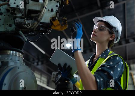 A female engineer installs a program on a robotics arm in a robot warehouse. And test the operation before sending the machine t Stock Photo