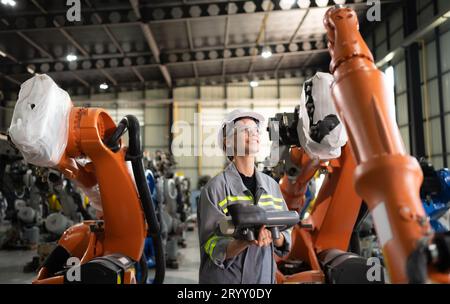 After installing a program on the robotic arm, a female engineer with a robotic arm controller performs a test run. Stock Photo