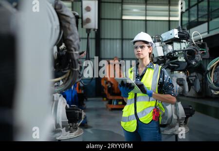A female engineer installs a program on a robotics arm in a robot warehouse. And test the operation before sending the machine t Stock Photo