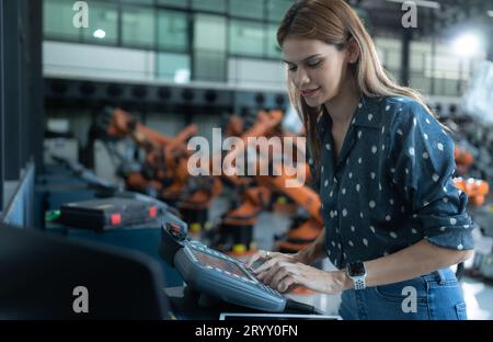 A female engineer installs a program on a robotics arm in a robot warehouse. And test the operation before sending the machine t Stock Photo