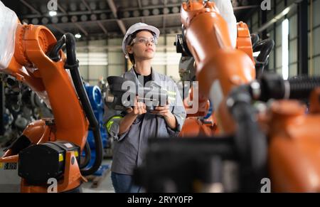 After installing a program on the robotic arm, a female engineer with a robotic arm controller performs a test run. Stock Photo