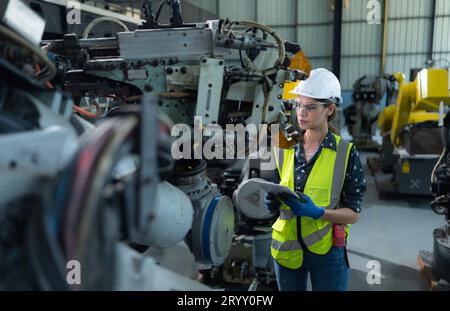 A female engineer installs a program on a robotics arm in a robot warehouse. And test the operation before sending the machine t Stock Photo