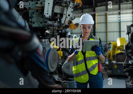 A female engineer installs a program on a robotics arm in a robot warehouse. And test the operation before sending the machine t Stock Photo