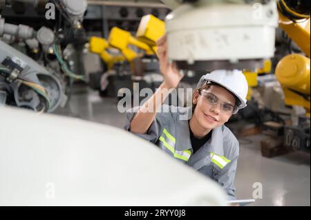 A female engineer installs a program on a robotics arm in a robot warehouse. And test the operation before sending the machine t Stock Photo