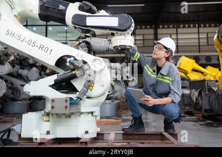 A female engineer installs a program on a robotics arm in a robot warehouse. And test the operation before sending the machine t Stock Photo