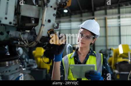A female engineer installs a program on a robotics arm in a robot warehouse. And test the operation before sending the machine t Stock Photo