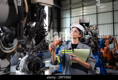 A female engineer checking documented items after installing a program on a robotic arm in a robotic warehouse and test the oper Stock Photo
