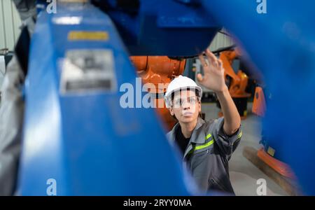 A female engineer installs a program on a robotics arm in a robot warehouse. And test the operation before sending the machine t Stock Photo