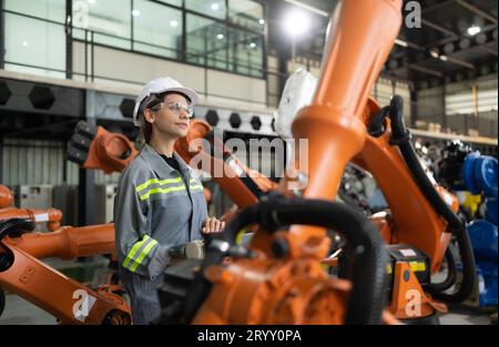 After installing a program on the robotic arm, a female engineer with a robotic arm controller performs a test run. Stock Photo