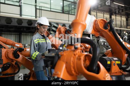 After installing a program on the robotic arm, a female engineer with a robotic arm controller performs a test run. Stock Photo