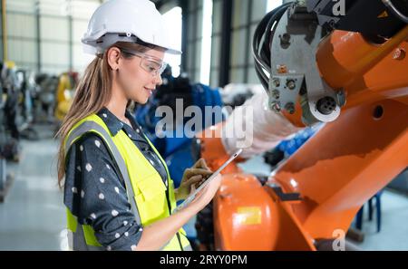 A female engineer installs a program on a robotics arm in a robot warehouse. And test the operation before sending the machine t Stock Photo