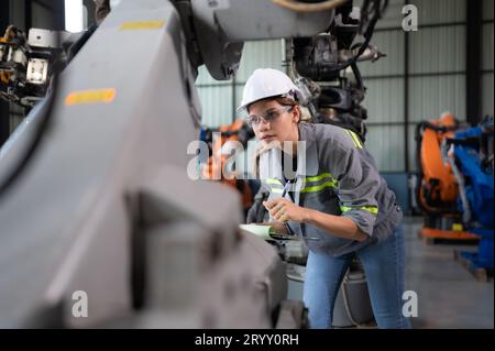 A female engineer checking documented items after installing a program on a robotic arm in a robotic warehouse and test the oper Stock Photo
