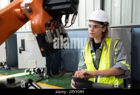 After installing a program on the robotic arm, a female engineer with a robotic arm controller performs a test run. Stock Photo