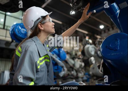 A female engineer installs a program on a robotics arm in a robot warehouse. And test the operation before sending the machine t Stock Photo