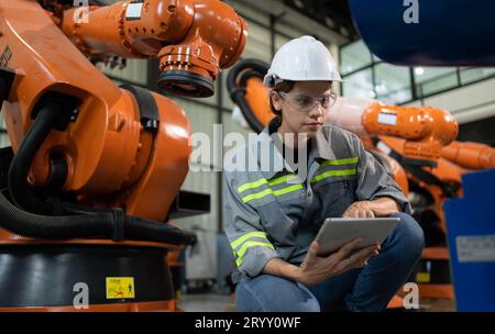 A female engineer installs a program on a robotics arm in a robot warehouse. And test the operation before sending the machine t Stock Photo