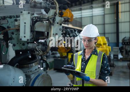 A female engineer installs a program on a robotics arm in a robot warehouse. And test the operation before sending the machine t Stock Photo