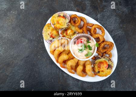 PERUVIAN FOOD. Piqueo caliente. Hot seafood platter fried shrimps, squid rings and baked scallops with sauce Stock Photo