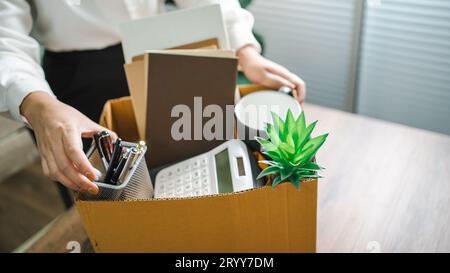 Business woman sending resignation letter and packing Stuff Resign Depress or carrying business cardboard box by desk in office. Stock Photo