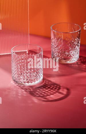 Two empty glass glasses on colored backgrounds with shadows from sunlight Stock Photo