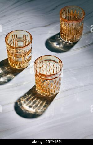 Three empty glass glasses on light background with shadows from sunlight Stock Photo