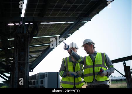 A team of electrical engineers is inspecting and maintaining solar panels at a solar panel site in the middle of a hundred acre Stock Photo