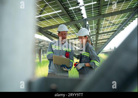 A team of electrical engineers is inspecting and maintaining solar panels at a solar panel site in the middle of a hundred acre Stock Photo