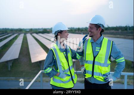 A team of electrical engineers inspecting solar panels in a hundred acres of grass on the rooftop of energy storage station, in Stock Photo