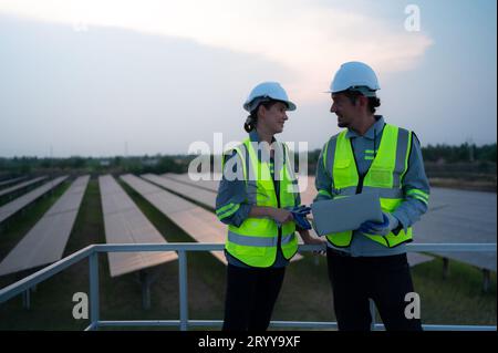 A team of electrical engineers inspecting solar panels in a hundred acres of grass on the rooftop of energy storage station, in Stock Photo