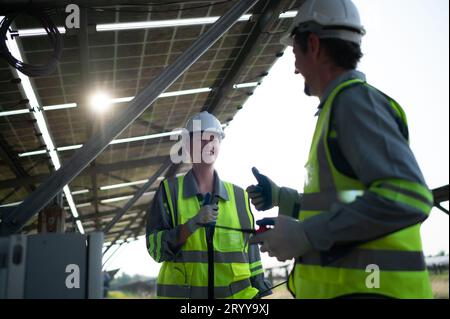 A team of electrical engineers is inspecting and maintaining solar panels at a solar panel site in the middle of a hundred acre Stock Photo