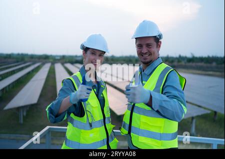 A team of electrical engineers inspecting solar panels in a hundred acres of grass on the rooftop of energy storage station, in Stock Photo