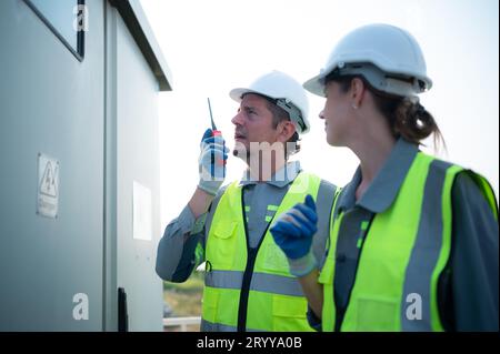A team of electrical engineers is inspecting an energy storage station of a solar panels in the middle of a hundred acre field o Stock Photo