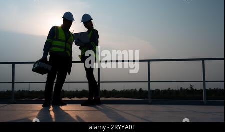 A team of electrical engineers inspecting solar panels in a hundred acres of grass on the rooftop of energy storage station, in Stock Photo