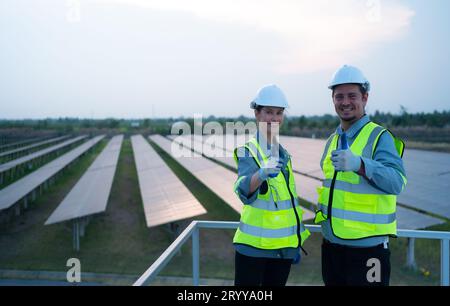 A team of electrical engineers inspecting solar panels in a hundred acres of grass on the rooftop of energy storage station, in Stock Photo