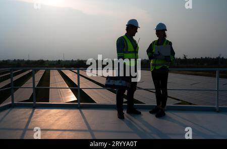 A team of electrical engineers inspecting solar panels in a hundred acres of grass on the rooftop of energy storage station, in Stock Photo
