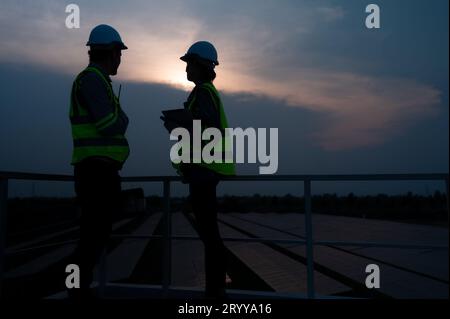 A team of electrical engineers inspecting solar panels in a hundred acres of grass on the rooftop of energy storage station, in Stock Photo