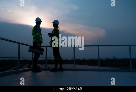 A team of electrical engineers inspecting solar panels in a hundred acres of grass on the rooftop of energy storage station, in Stock Photo