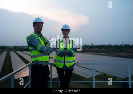 A team of electrical engineers inspecting solar panels in a hundred acres of grass on the rooftop of energy storage station, in Stock Photo
