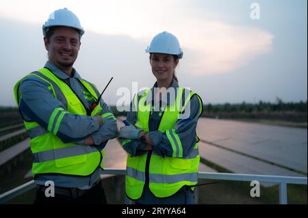 A team of electrical engineers inspecting solar panels in a hundred acres of grass on the rooftop of energy storage station, in Stock Photo