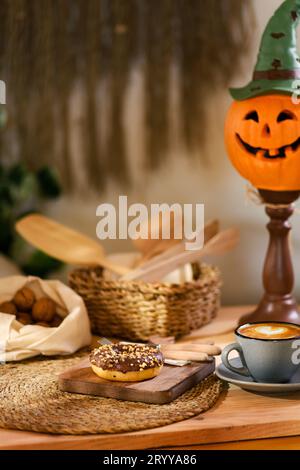 A single donut rests on a wooden plate, with walnuts on a white cloth behind. In a wicker basket, wooden kitchen tools lay, alongside a latte and a ja Stock Photo