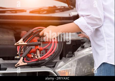 Closeup of woman hand holding battery cable copper wire for repairing broken car by connect battery with red and black line to e Stock Photo