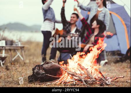 Closeup of bonfire and friendship clinking drinking bottle glass for celebrating in party with mountain meadow and lake view bac Stock Photo