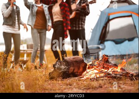 Closeup of campfire and friendship dancing to beat of the music for celebrating in party with mountain meadow and lake view back Stock Photo