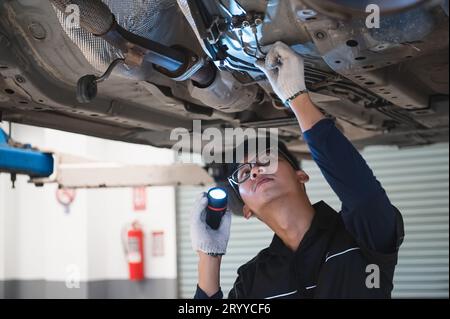 Asian male mechanical hold and shining flashlight to examine car disk
