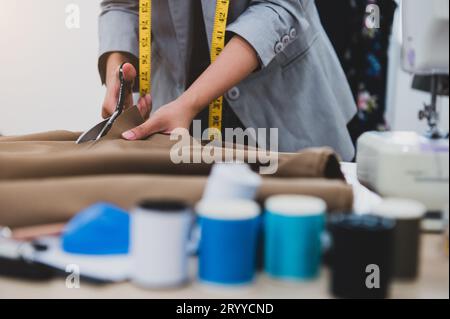 Dressmaker cutting dress fabric on sketch line with colorful thread foreground. Fashion designer tailor or sewer in workshop stu Stock Photo