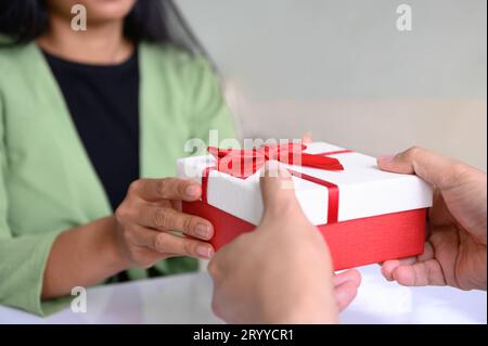 Closeup of hands giving gift box in Christmas day and new year festival to each other with woman background. Holiday and event. Stock Photo