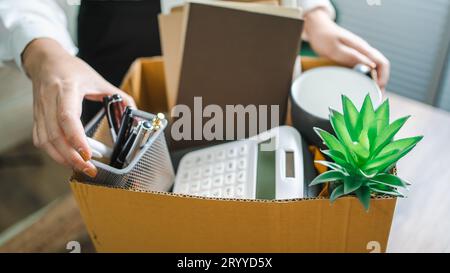 Business woman sending resignation letter and packing Stuff Resign Depress or carrying business cardboard box by desk in office. Stock Photo