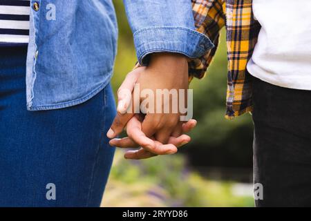 Midsection of diverse couple holding hands, walking in garden Stock Photo