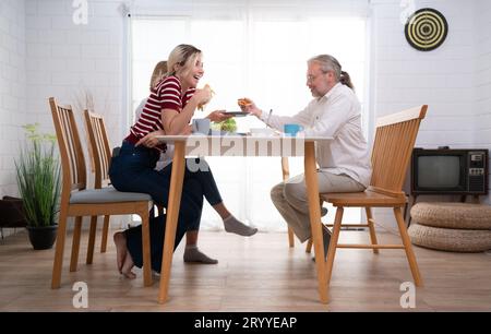 The father, mother, and daughter are delighted to eat dinner together at the family table. Stock Photo