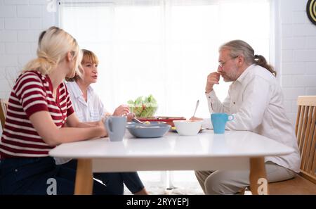 The father, mother, and daughter are delighted to eat dinner together at the family table. Stock Photo