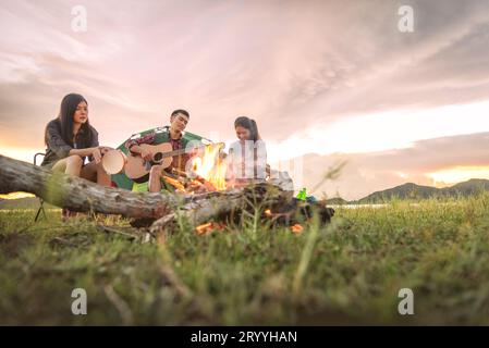 Group of travelers camping and doing picnic and playing music together. Mountain and lake background. People and lifestyle. Outd Stock Photo